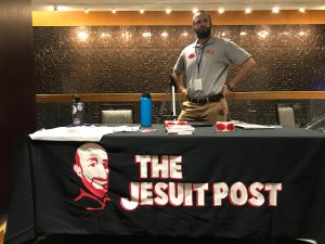 Brian Strassburger of the Jesuit Post sits at an information table at a conference
